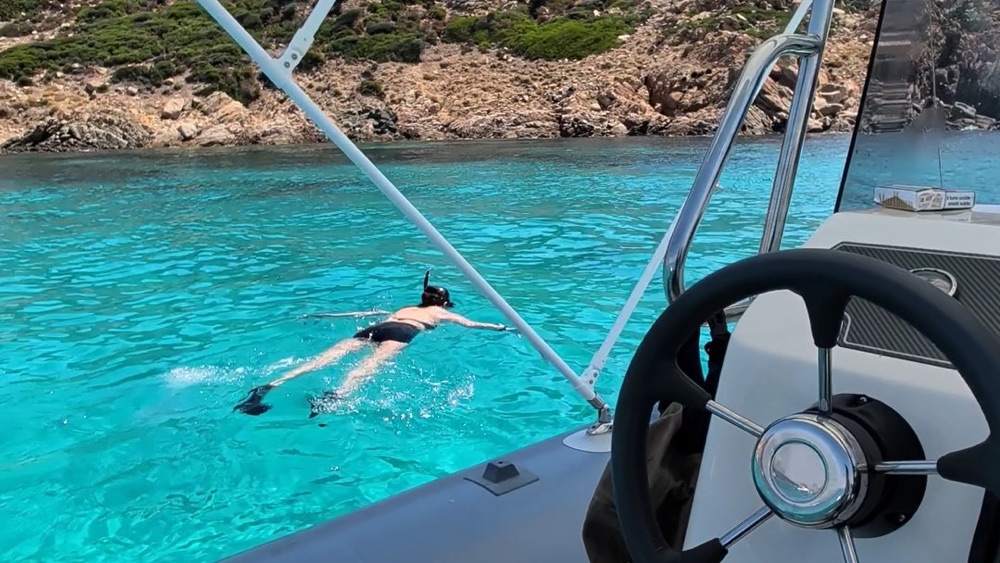 Snorkelling in turquoise water off a rocky Sardinian island, seen from a rented boat